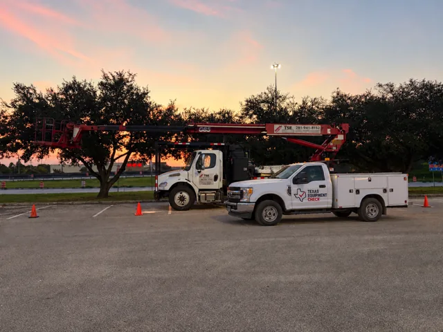 A branded Texas Equipment Check bucket truck and service truck parked at a jobsite at dusk