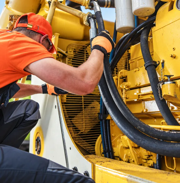 A Texas Equipment Check inspector closely examining hydraulic hoses and fittings on a piece of yellow equipment during an inspection